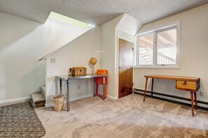A room with a carpeted floor, a desk, a chair, a wooden cabinet, a globe, and a window with a view of a wooden structure outside. - Ridge View - Mountain Top Home with 360 Views (Estes Park)