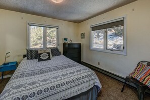 A bedroom with a bed, two windows, a dresser, a chair, and a desk.