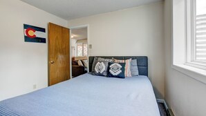 A bedroom with a bed, a door, a window, and a wall-mounted artwork.
