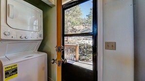 A laundry room with a washer and dryer, a window with a view of trees and rocks, and a door with a wooden railing.