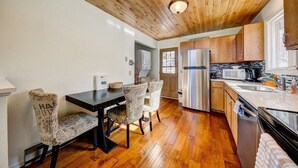 A kitchen with wooden ceiling, a dining table with chairs, a refrigerator, and a microwave.