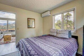 Une chambre à coucher comprenant un lit, une commode, un miroir et une fenêtre donnant sur des arbres et des montagnes.