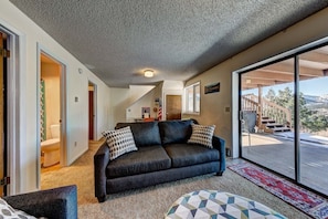 A living room with a dark sofa, a patterned rug, and a view of a mountainous landscape through large sliding glass doors.