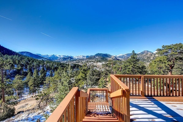 A wooden staircase leading to a deck with a view of snow-capped mountains and a forested valley.