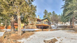 A large stone house with a wooden deck and a green roof, surrounded by trees and snow. - Stone's Throw - A Downtown Estes Park getaway (Estes Park)