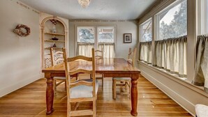 A dining room with a wooden table and chairs, a chandelier, and a window with curtains. - Stone's Throw - A Downtown Estes Park getaway (Estes Park)