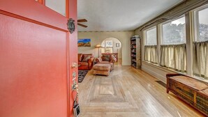 A spacious living room with a wooden parquet floor, a red door, and a large window with curtains. - Stone's Throw - A Downtown Estes Park getaway (Estes Park)