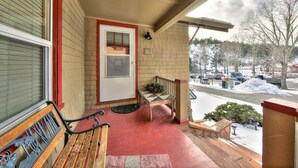 A covered porch with a bench, a door, and a view of a snowy parking lot. - Stone's Throw - A Downtown Estes Park getaway (Estes Park)