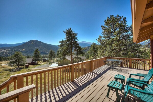 Une terrasse en bois avec des meubles d’extérieur, une vue sur les montagnes et un ciel dégagé.