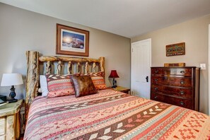 Une chambre à coucher avec un grand lit, une tête de lit en bois, une commode, une table de chevet avec une lampe et un tableau encadré au mur.