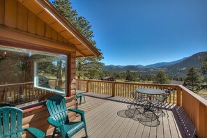 Une terrasse en bois avec une table et des chaises, offrant une vue sur un paysage montagneux.