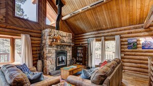 A log cabin interior with a stone fireplace, wooden walls, and a cozy seating area. - Windham Drive - Beautiful Secluded Mountain Home (Estes Park)