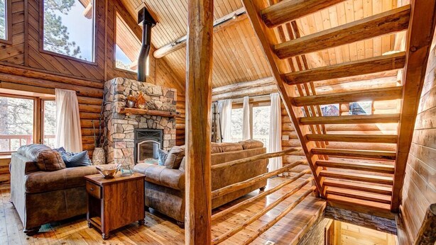 A log cabin interior with a stone fireplace, wooden beams, and a cozy seating area. - Windham Drive - Beautiful Secluded Mountain Home (Estes Park)