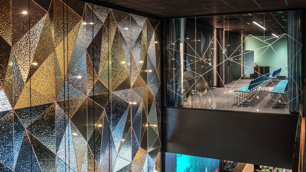 A modern interior with geometric wall patterns, a seating area with tables and chairs, and a view through a glass partition. - Thon Hotel Snø (Lorenskog)