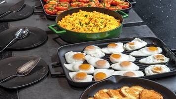 Un bufé de desayuno con diversos platos, incluyendo huevos, tortitas y tortillas.