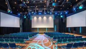 A large auditorium with rows of chairs, a stage with a large screen, and overhead lighting. - Thon Hotel Snø (Lorenskog)