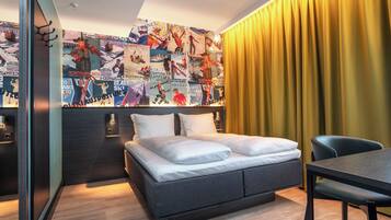 A modern hotel room with a bed, a dining table, and a wall decorated with posters.