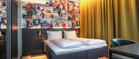 Una habitación de hotel moderna con una cama, una mesa de comedor y una pared decorada con carteles.