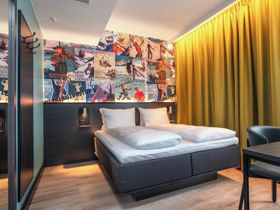 A modern hotel room with a bed, a dining table, and a wall decorated with posters.