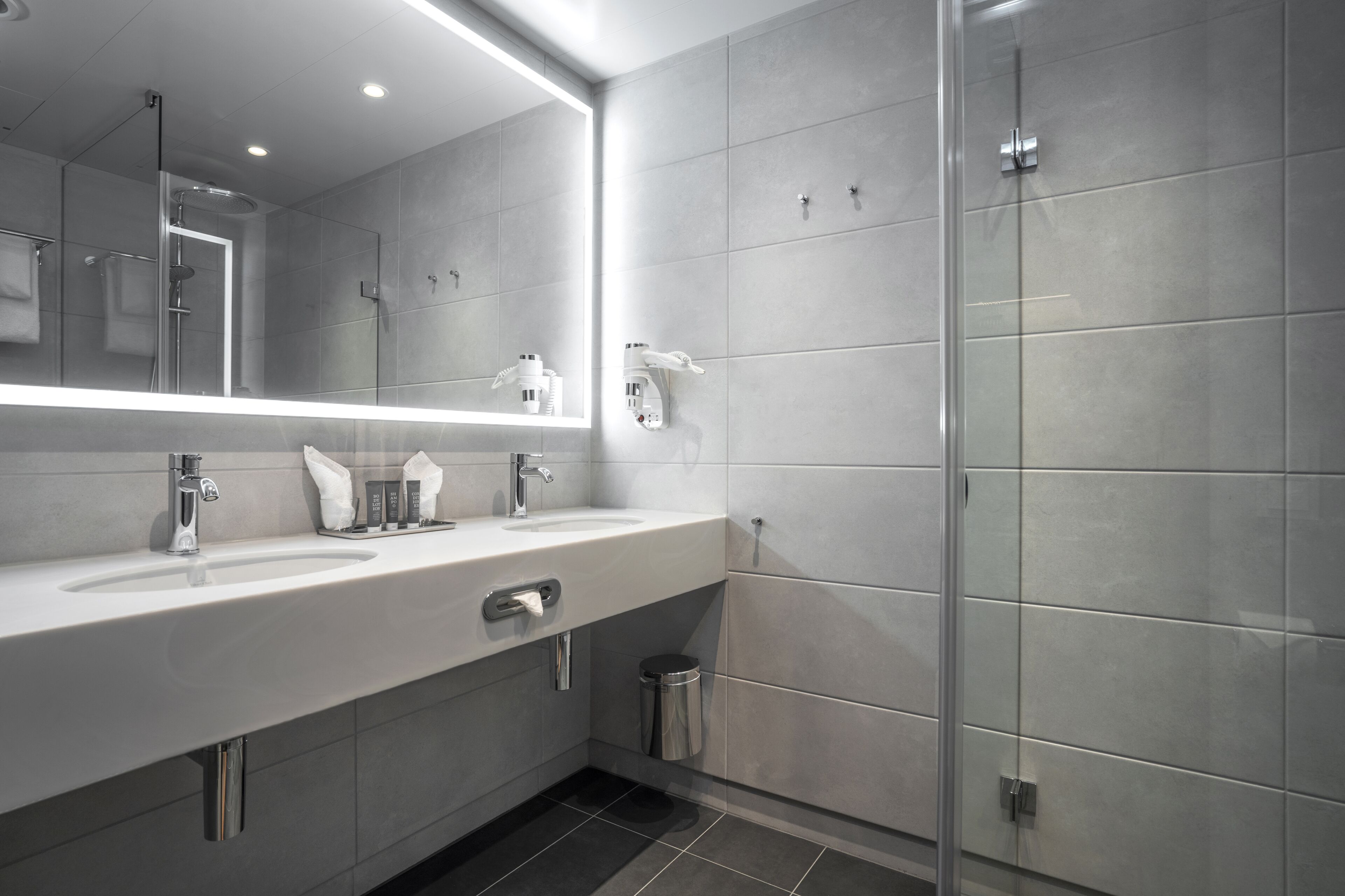 Un bagno moderno con uno specchio grande, un lavandino, una doccia e un cestino.