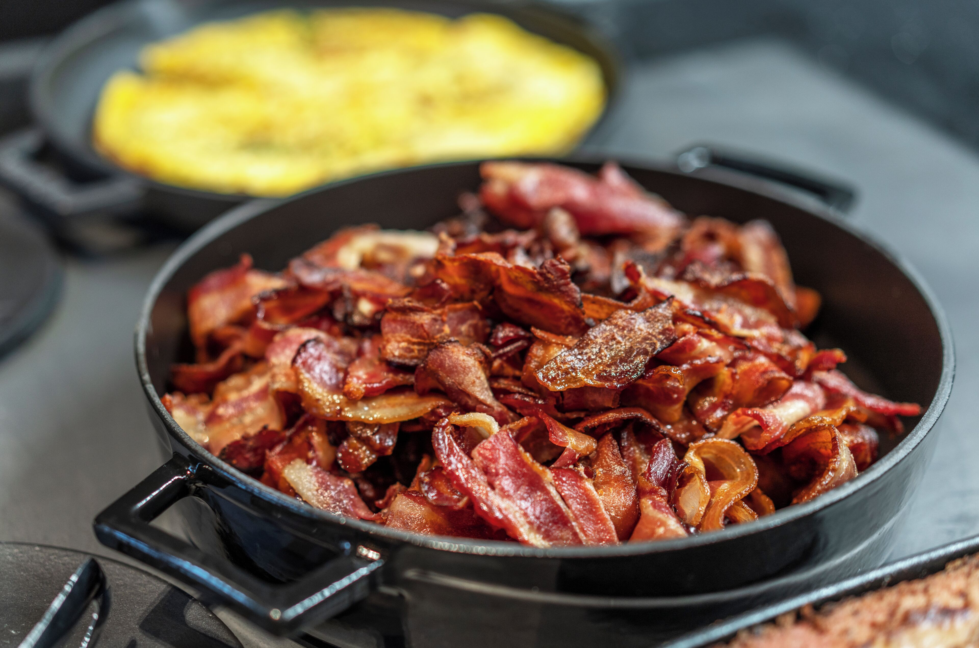 A skillet with cooked bacon and a pan of fried eggs.