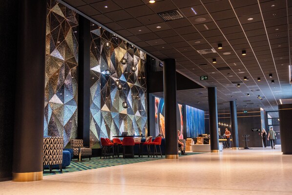 A modern hotel lobby with geometric wall patterns, red and patterned seating, and a reception area.