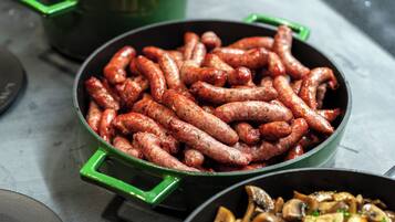 A close-up of cooked sausages in a green pan, with a bowl of mushrooms in the foreground.