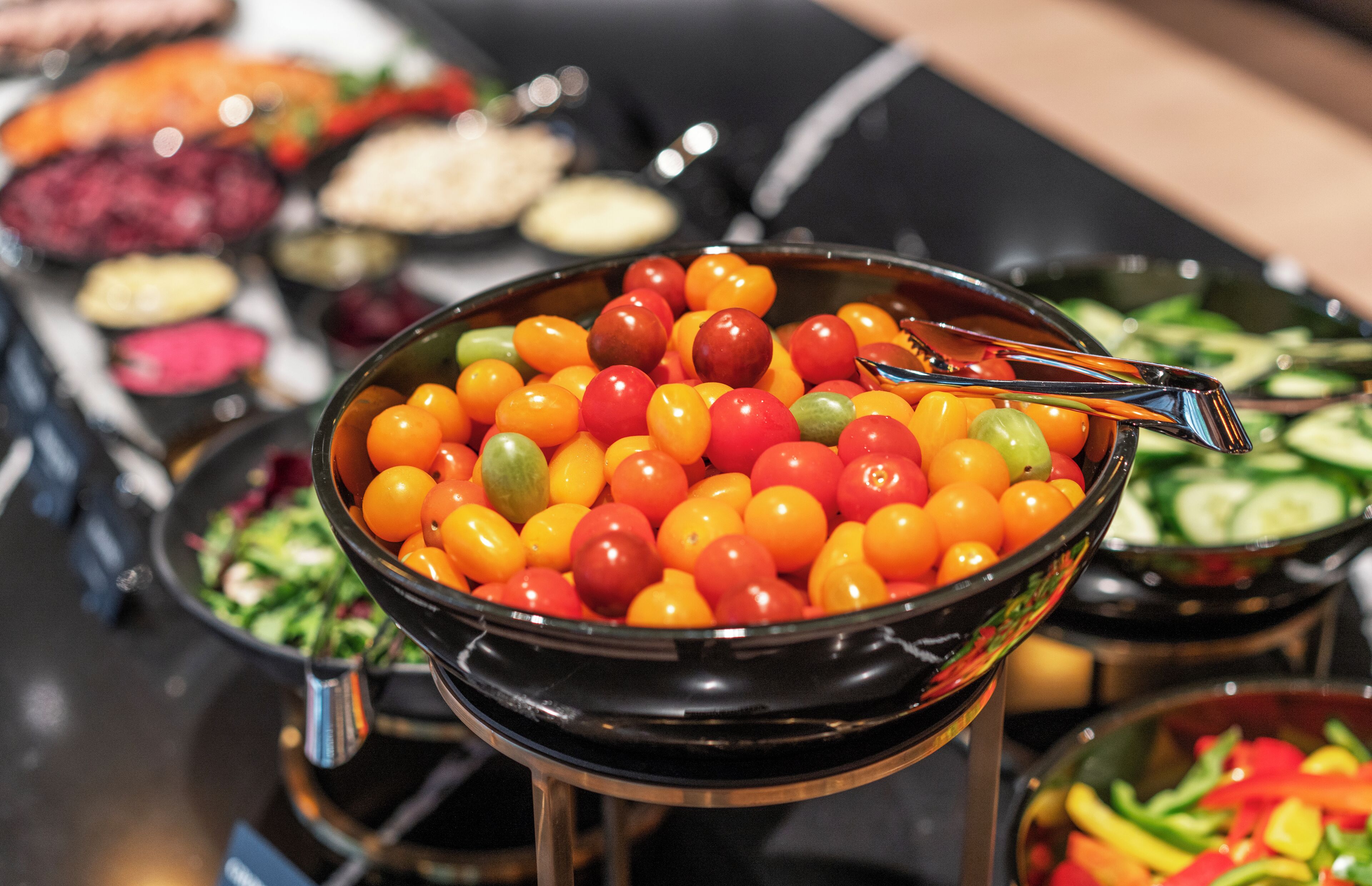 Un bufé con una variedad de platos, incluyendo un bol de tomates cherry, ensaladas y otros alimentos preparados.