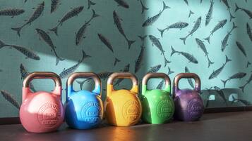 Cinco kettlebells de diferentes colores alineados contra una pared con un estampado de peces.