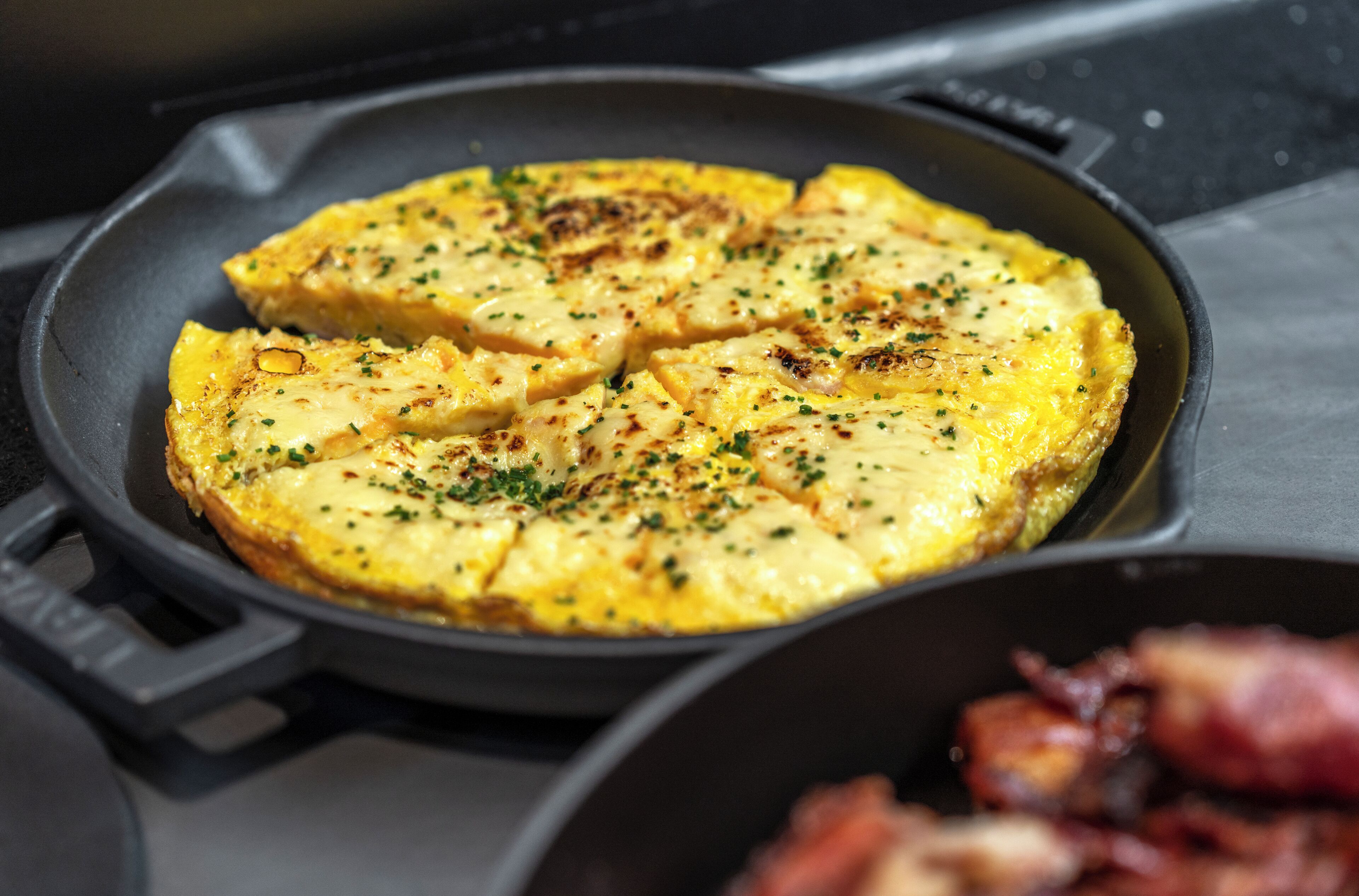 Une poêle contenant un plat cuisiné, peut-être une frittata, garnie d’herbes.