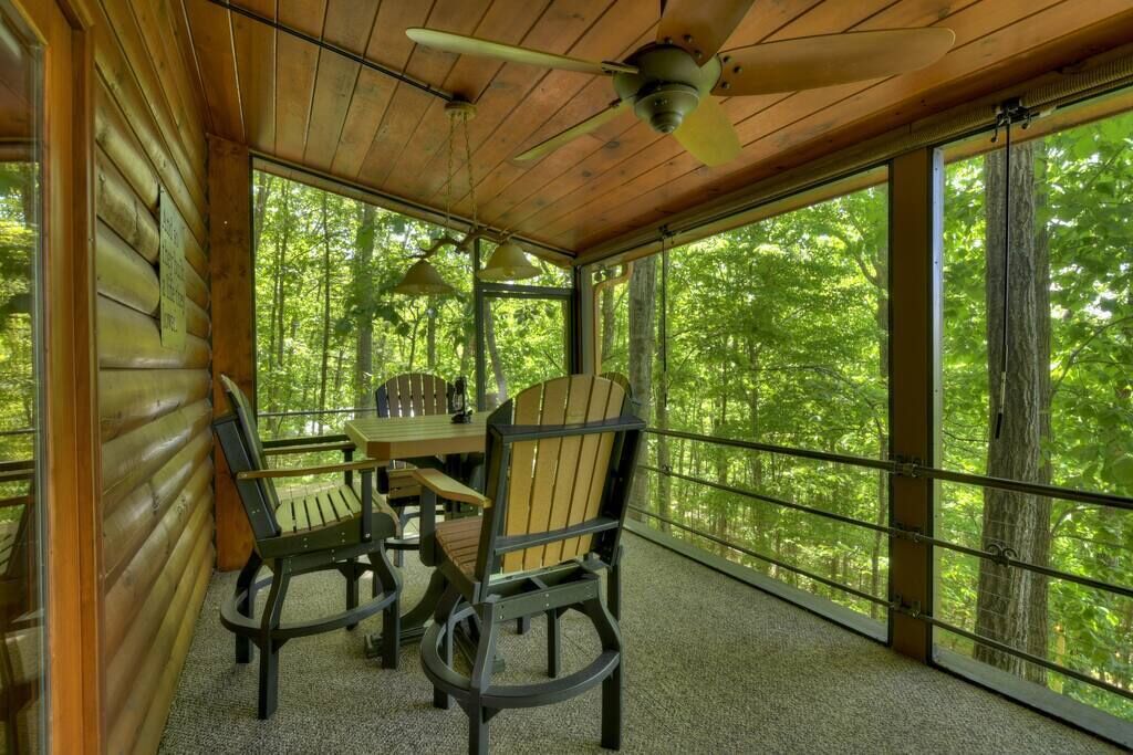 A wooden cabin with a dining table and chairs, large windows, and a ceiling fan.