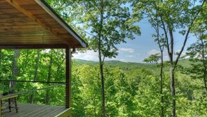 A wooden cabin with a balcony overlooking a dense forest and distant hills. - Cedar Ridge | Hot Tub + Game Room + Fire Pit (Blue Ridge)