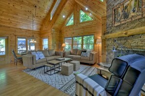 A spacious log cabin interior with a high ceiling, large windows, and a stone fireplace. - Cedar Ridge | $199 Off Your Stay! (Blue Ridge)
