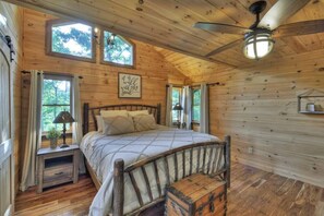 A wooden cabin bedroom with a bed, a nightstand, a chest of drawers, and a ceiling fan.