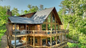 Une cabane en bois à deux étages, dotée d’un balcon et d’une terrasse, entourée d’arbres.