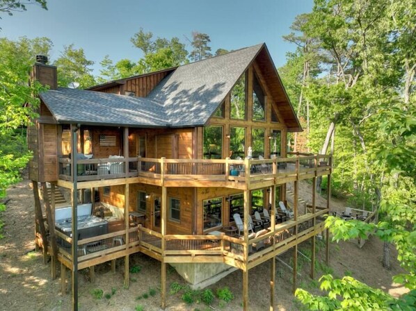 A two-story wooden cabin with a balcony and deck, surrounded by trees.