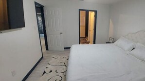 A bedroom with a large bed, a door leading to another room, and a patterned carpet.
