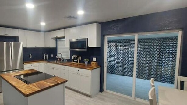 A modern kitchen with white cabinets, a stainless steel refrigerator, and a wooden countertop.