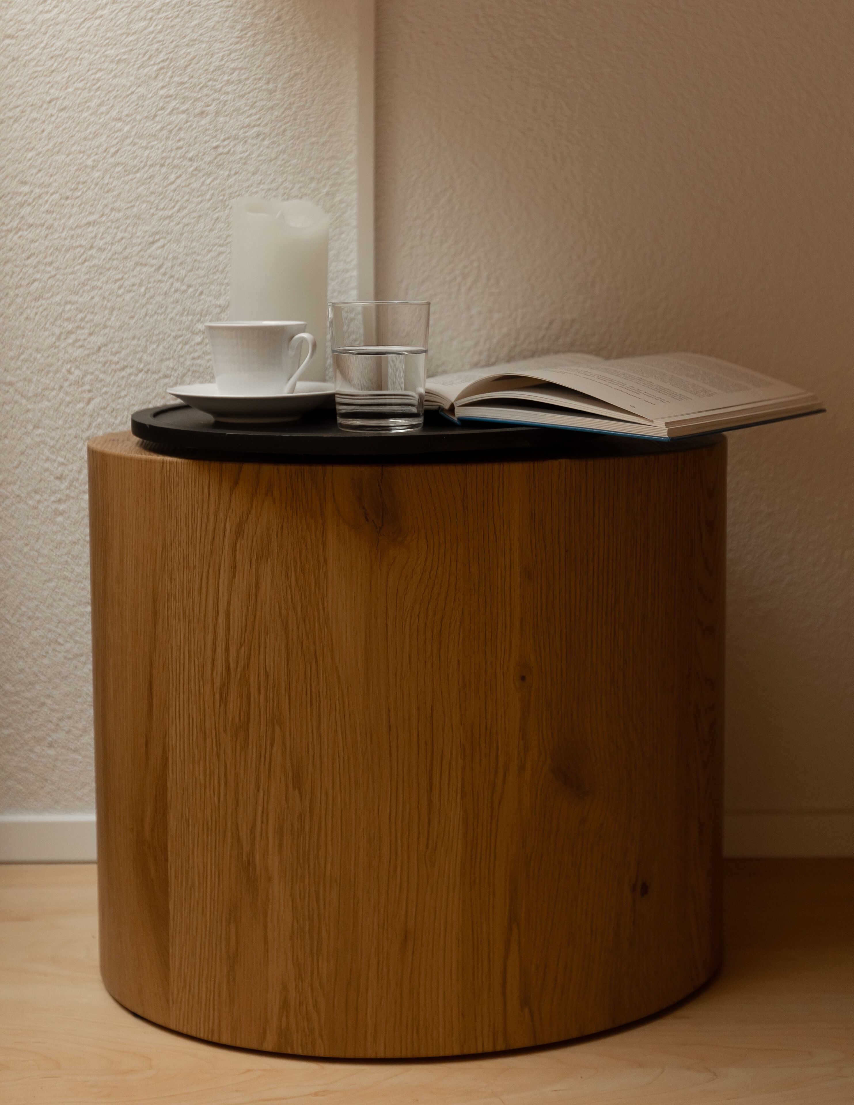 Une petite table d’appoint en bois, sur laquelle se trouvent un livre, un verre d’eau et une tasse blanche.