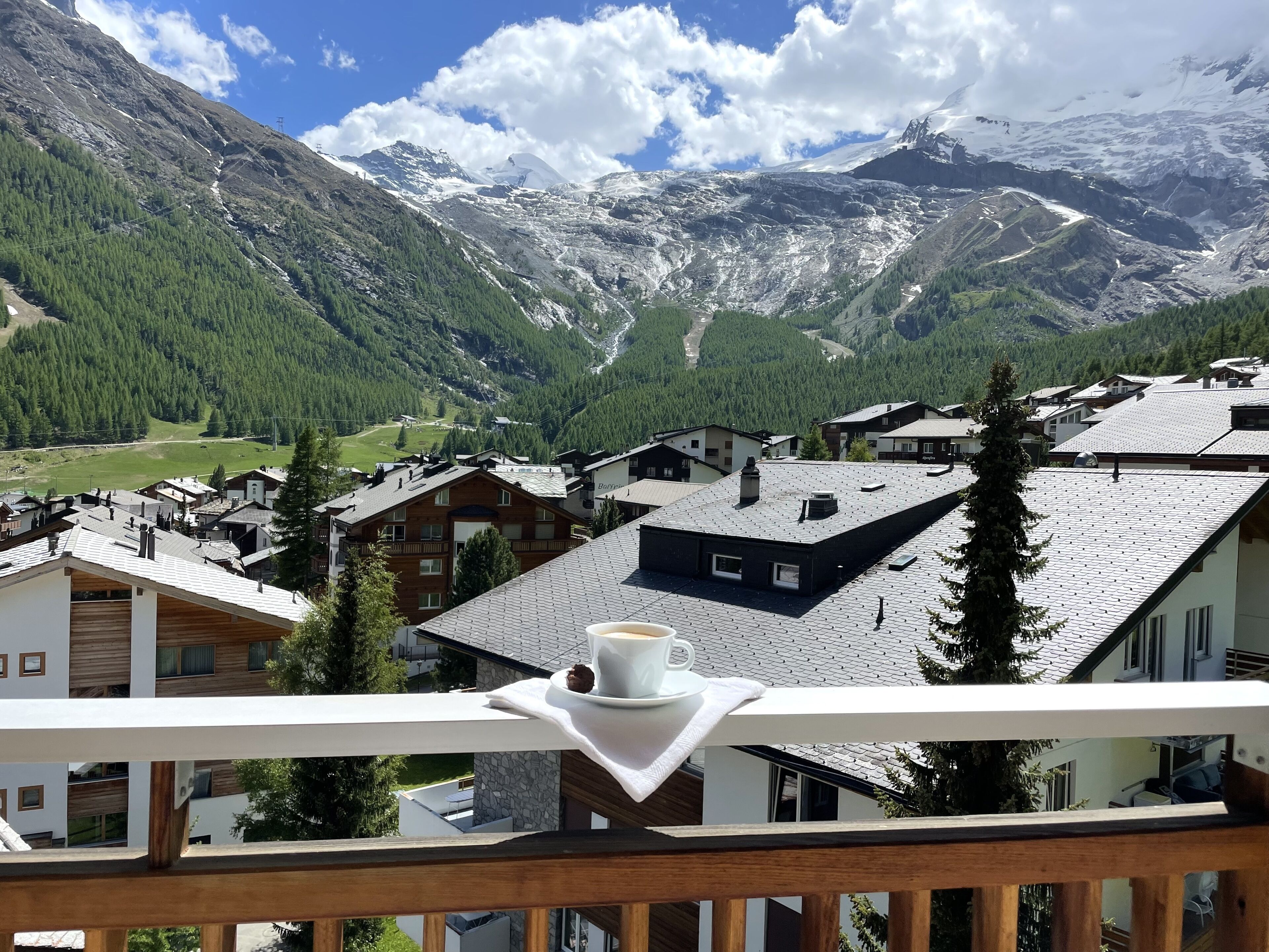 Ein Bergdorf mit traditionellen Holzhäusern, einem Balkon mit Tasse und Untertasse und Blick auf schneebedeckte Gipfel.