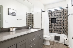 A modern bathroom with a grey vanity, a toilet, and a shower with patterned tiles.