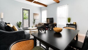Ein modernes Wohnzimmer mit einem dunklen Sofa, einem Esstisch und einem Fernseher.