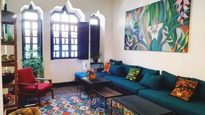 A living room with a blue sofa, a red chair, a colorful patterned rug, and a large abstract painting on the wall. - La Banksia Hotel (Quito)