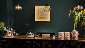 A bar area with a framed sign reading "La Banksia HOTEL QUILTO", a tea set, a speaker, and decorative vases. - La Banksia Hotel (Quito)
