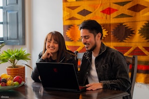 Two people sitting at a table with a laptop, a potted plant, and a bowl of fruit. - La Banksia Hotel (Quito)