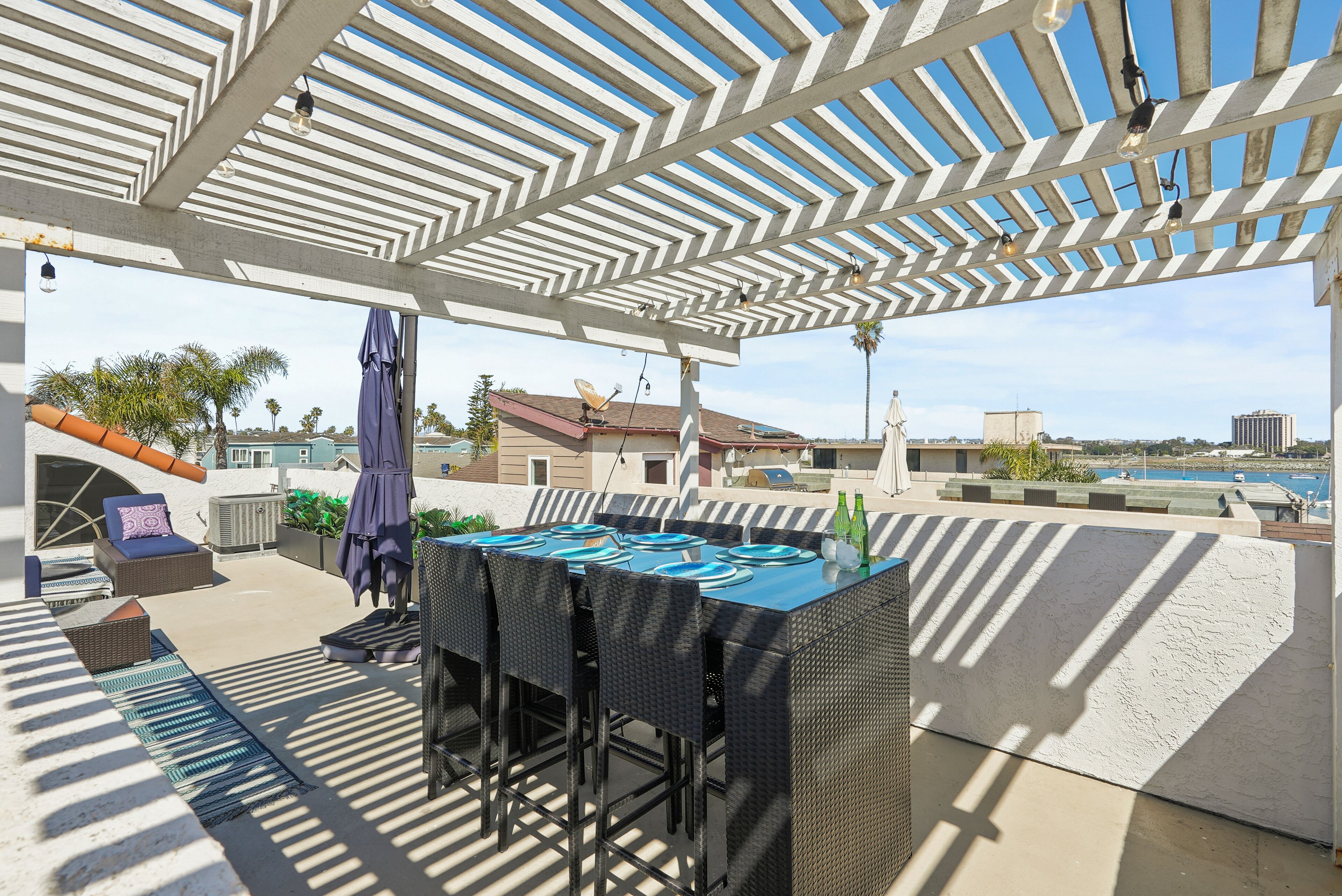 Un patio al aire libre con zona de estar techada, bar y piscina al fondo.