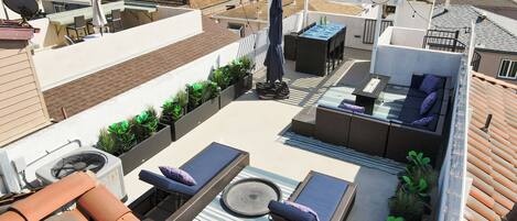 A rooftop terrace with outdoor furniture, a fan, and potted plants.