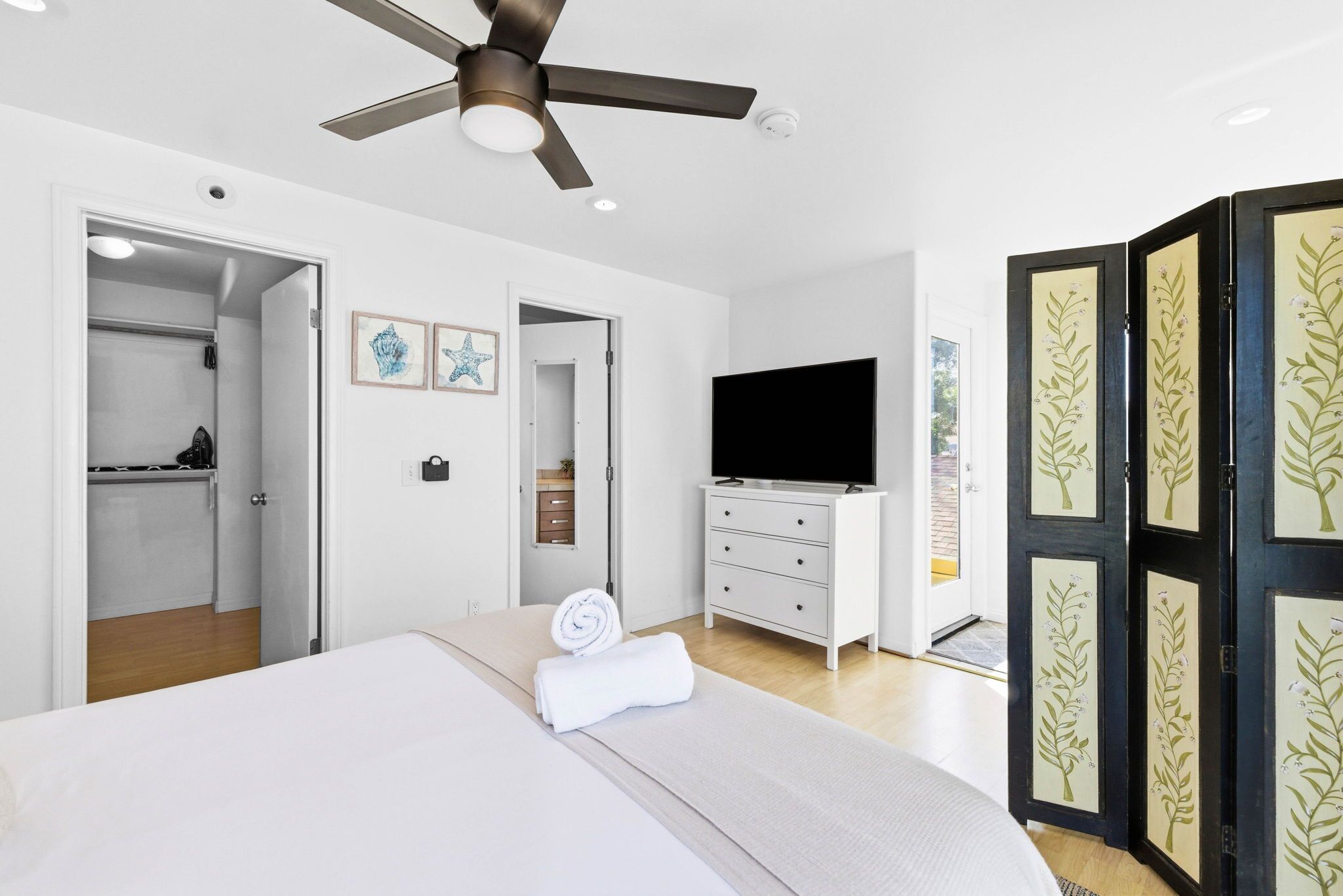 Une chambre à coucher comprenant un lit, un ventilateur de plafond, une télévision, une armoire et une porte ornée de panneaux décoratifs.
