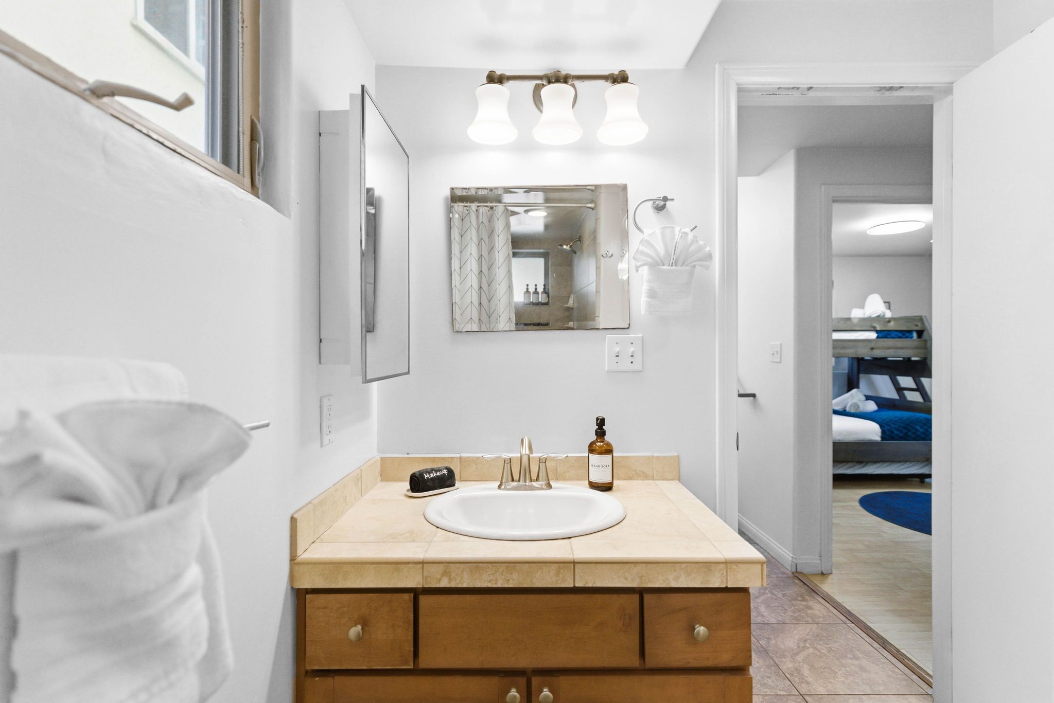 A bathroom with a sink, mirror, and vanity. There is a towel rack and a bottle on the counter.