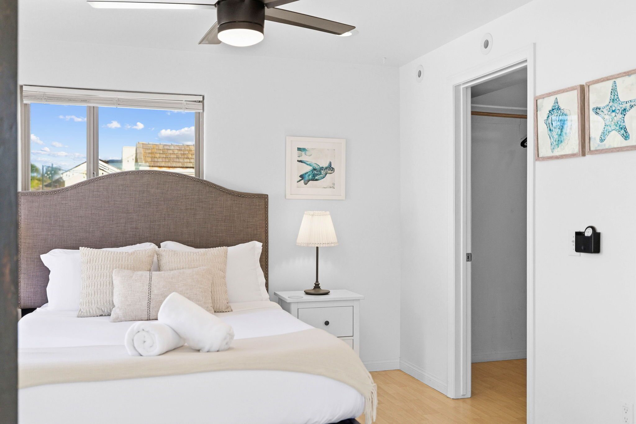 A neatly made bed with a headboard, a bedside lamp, and a window with blinds.